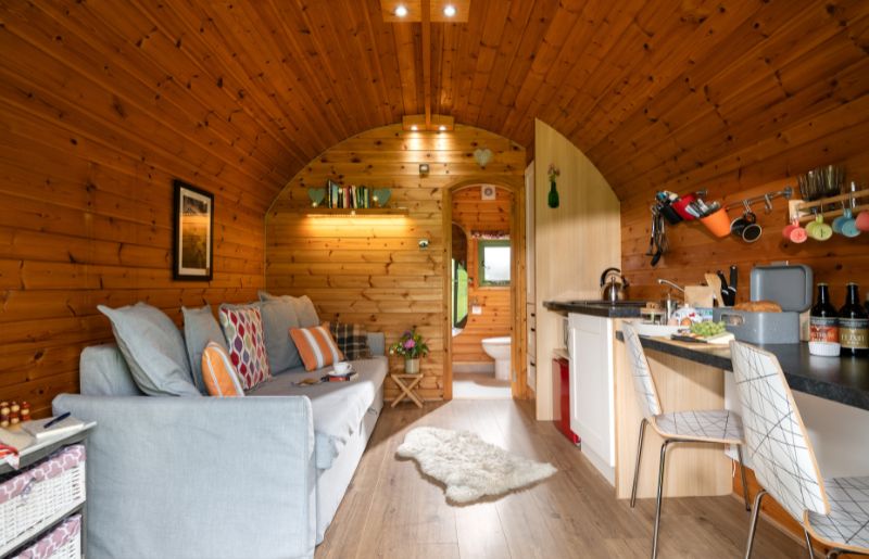A comfy grey sofa and a kitchenette, with a view through an open door at the back onto a bathroom